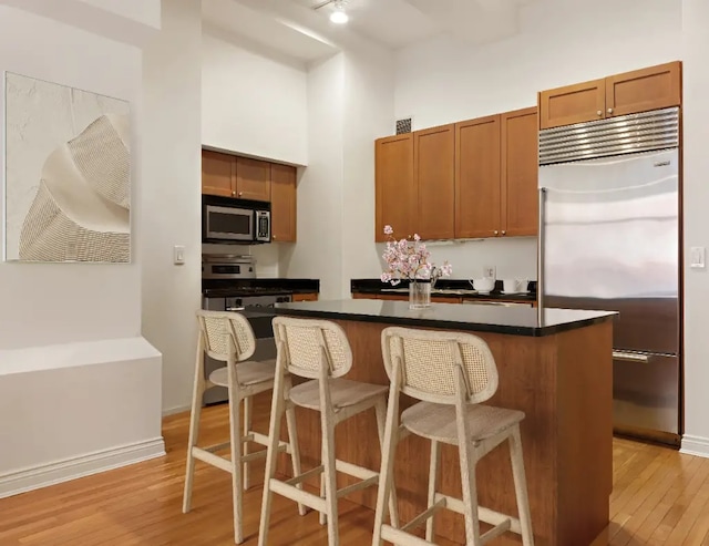 252 7th Ave Unit 5T, New York City, NY 10001 - kitchen featuring appliances with stainless steel finishes, light wood-style flooring, dark countertops, a kitchen island, and a breakfast bar