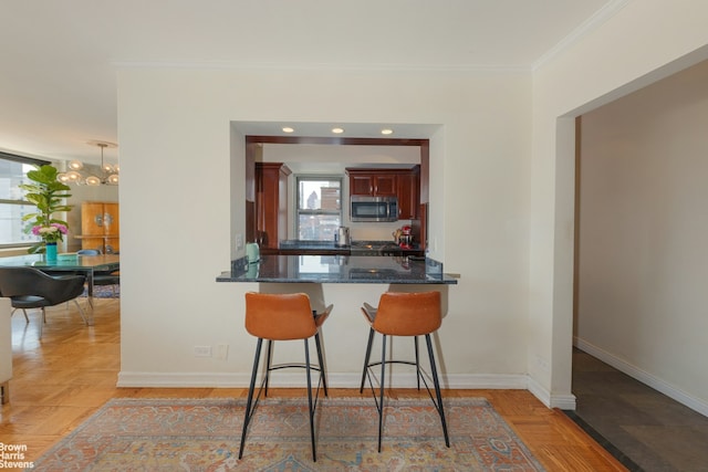 500 E 83rd St Unit 16M, New York City, NY 10028 - kitchen with stainless steel microwave, crown molding, a breakfast bar, dark stone counters, and reddish brown cabinets
