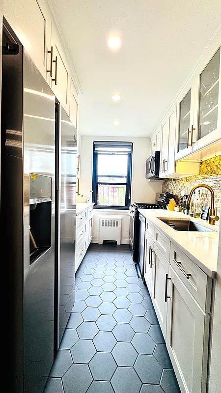90-09 Northern Blvd Unit 504, New York City, NY 11372 - kitchen featuring radiator heating unit, appliances with stainless steel finishes, a sink, light countertops, and glass insert cabinets