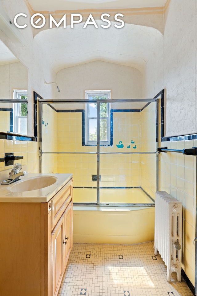 536 E 43rd St, New York City, NY 11203 - bathroom with radiator, healthy amount of natural light, vanity, bath / shower combo with glass door, and tile walls