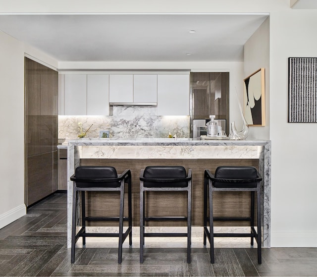 303 Park Ave Unit 2022, New York City, NY 10022 - kitchen with white cabinets, a breakfast bar, backsplash, and modern cabinets