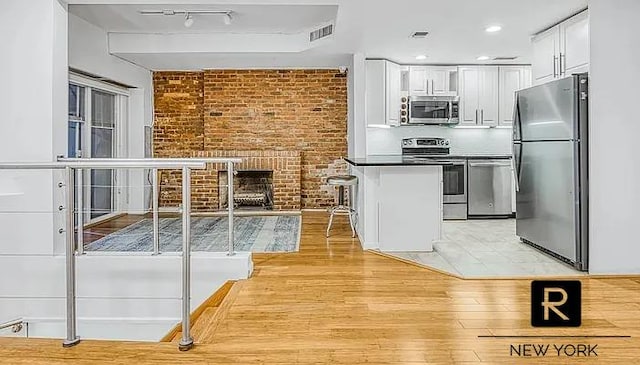 233 E 31st St Unit A, New York City, NY 10016 - kitchen featuring appliances with stainless steel finishes, brick wall, white cabinetry, a peninsula, and a fireplace