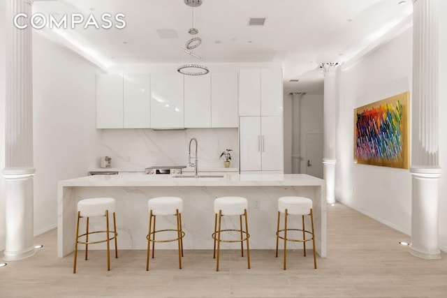 63 Greene St Unit 2D, New York City, NY 10012 - kitchen featuring modern cabinets, a sink, white cabinets, ornate columns, and decorative light fixtures