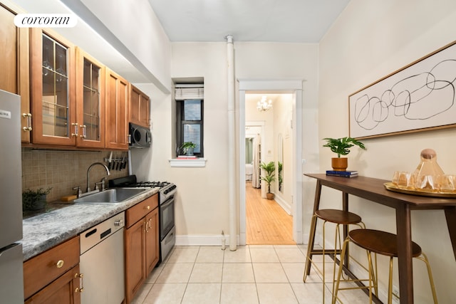 62 E 87th St Unit 1B, New York City, NY 10128 - kitchen with appliances with stainless steel finishes, a sink, brown cabinetry, tasteful backsplash, and glass insert cabinets