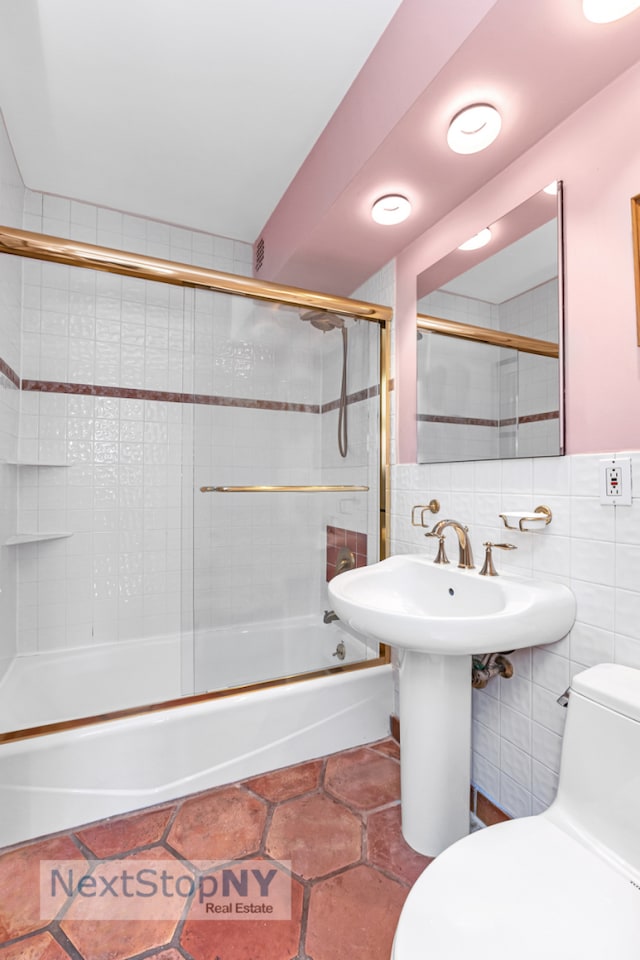 1175 York Ave Unit 16J, New York City, NY 10065 - full bath featuring toilet, bath / shower combo with glass door, tile walls, a sink, and tile patterned floors