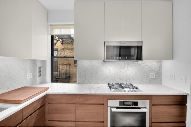 253 W 16th St Unit 6D, New York City, NY 10011 - kitchen with stainless steel appliances, modern cabinets, backsplash, and light stone counters