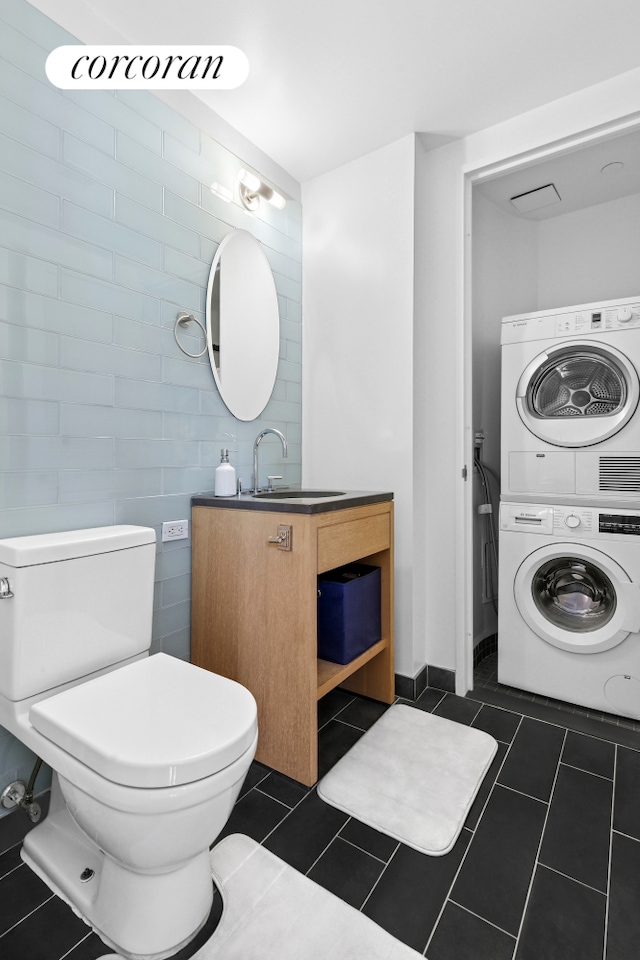 310 W 52nd St Unit 15A, New York City, NY 10019 - bathroom featuring stacked washer / dryer, vanity, tile walls, toilet, and tile patterned flooring