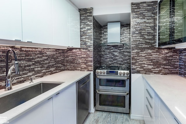 400 E 56th St Unit 27H, New York City, NY 10022 - kitchen with wall chimney exhaust hood, stainless steel appliances, backsplash, white cabinetry, and light wood finished floors
