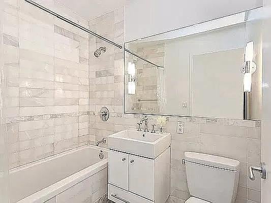 635 W 42nd St Unit 12M, New York City, NY 10036 - full bathroom featuring vanity, washtub / shower combination, and tile walls