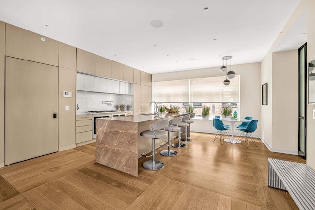 21 W 20th St Unit Ph1, New York City, NY 10011 - kitchen featuring a breakfast bar, a center island with sink, decorative backsplash, modern cabinets, and light wood finished floors
