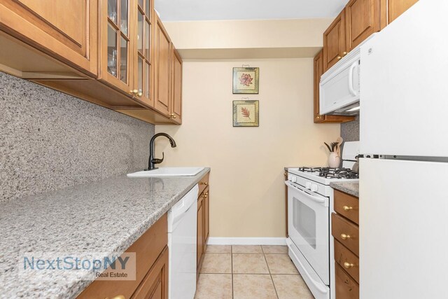 411 E 57th St Unit 2E, New York City, NY 10022 - kitchen featuring white appliances, light tile patterned floors, brown cabinetry, glass insert cabinets, and light stone countertops