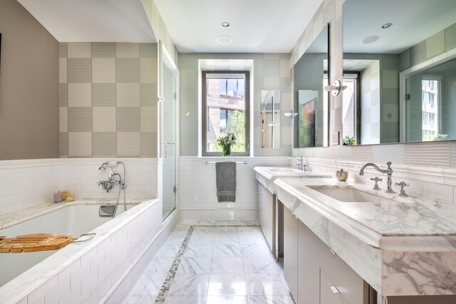 43 W 64th St Unit 6A, New York City, NY 10023 - bathroom featuring a garden tub, double vanity, marble finish flooring, a shower with door, and tile walls