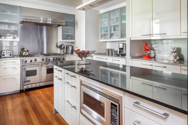 43 W 64th St Unit 6A, New York City, NY 10023 - kitchen featuring appliances with stainless steel finishes, wall chimney exhaust hood, tasteful backsplash, dark stone counters, and dark wood-style floors