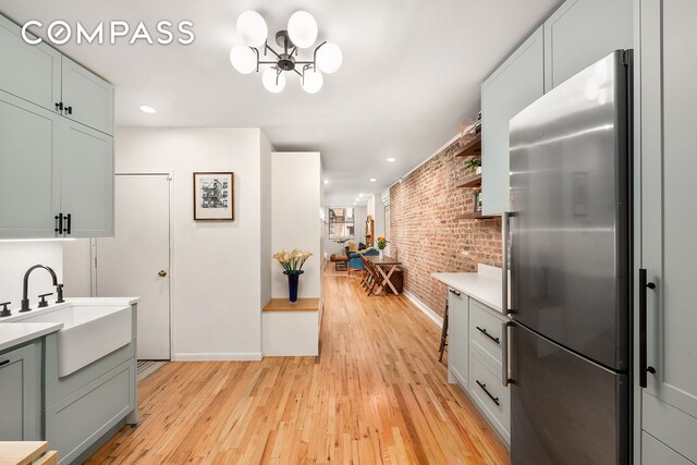 334 E 5th St Unit 2, New York City, NY 10003 - kitchen featuring stainless steel refrigerator, brick wall, a chandelier, light countertops, and light wood-type flooring