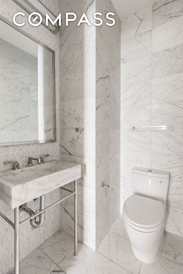 116 University Pl Unit 5, New York City, NY 10003 - half bath featuring marble tiled floors, toilet, tile walls, and stone wall
