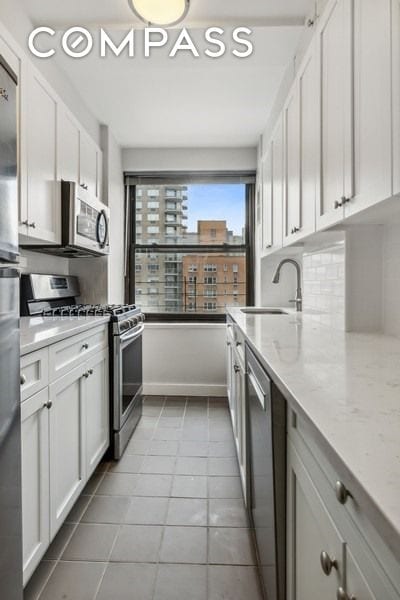235 E 73rd St Unit 12C, New York City, NY 10021 - kitchen with appliances with stainless steel finishes, white cabinetry, light tile patterned floors, and light stone counters