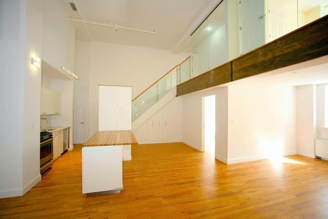 259 21st St Unit 1C, New York City, NY 11215 - unfurnished living room featuring a high ceiling, light wood finished floors, rail lighting, stairway, and a sink