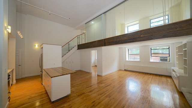 259 21st St Unit 1C, New York City, NY 11215 - unfurnished living room with a towering ceiling, light wood-type flooring, rail lighting, stairs, and healthy amount of natural light