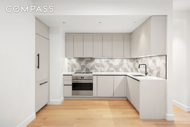 176 W 87th St Unit 1H, New York City, NY 10024 - kitchen with stainless steel appliances, modern cabinets, backsplash, and light wood finished floors