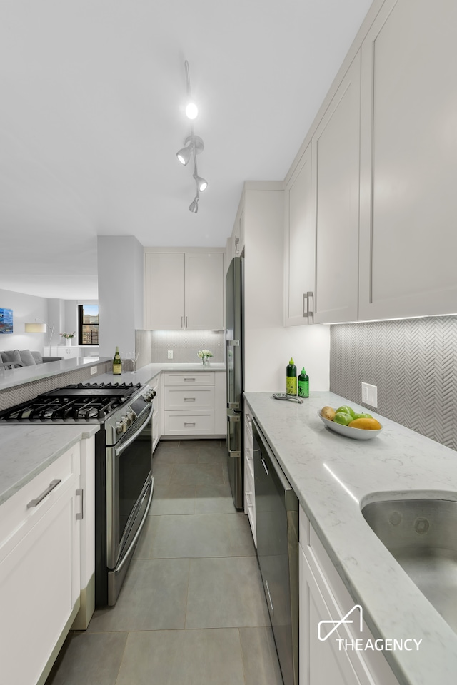 239 E 79th St Unit 12A, New York City, NY 10075 - kitchen with stainless steel appliances, tasteful backsplash, light stone countertops, white cabinets, and light tile patterned flooring