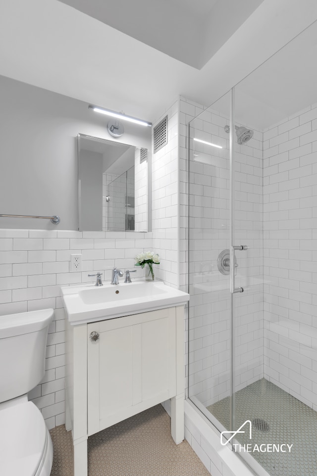 239 E 79th St Unit 12A, New York City, NY 10075 - bathroom with toilet, vanity, a shower stall, tile patterned floors, and tile walls