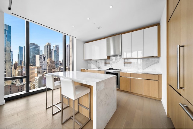 277 5th Ave Unit 25D, New York City, NY 10016 - kitchen with oven, modern cabinets, wall chimney range hood, light wood-type flooring, and backsplash