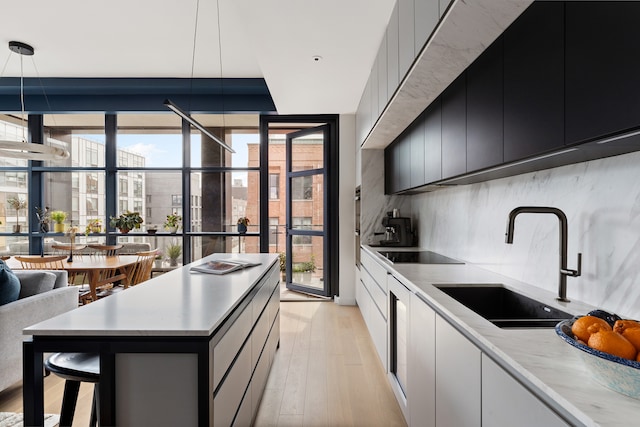 215 N 10th St Unit 4F, New York City, NY 11211 - kitchen with dark cabinets, a wall of windows, black electric cooktop, light countertops, and light wood-style flooring