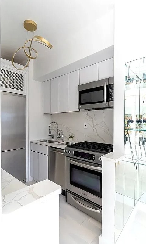 401 E 86th St Unit 18C, New York City, NY 10028 - kitchen with appliances with stainless steel finishes, a sink, decorative backsplash, light stone countertops, and white cabinetry