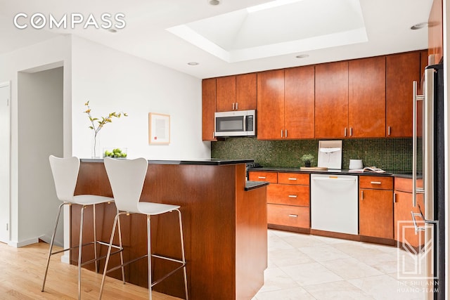 222 23rd St Unit C, New York City, NY 11232 - kitchen with appliances with stainless steel finishes, a raised ceiling, dark countertops, a breakfast bar, and decorative backsplash