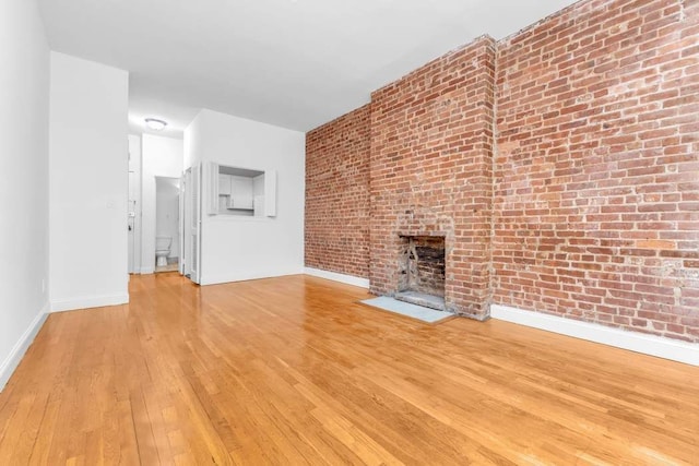 407 E 87th St Unit 3C, New York City, NY 10128 - unfurnished living room featuring hardwood / wood-style flooring, baseboards, a brick fireplace, and brick wall