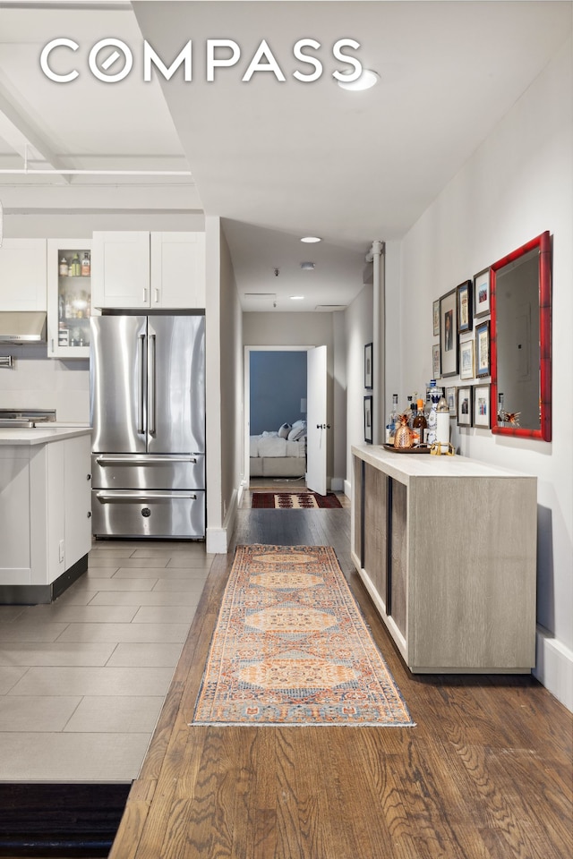 129 W 22nd St Unit 5A, New York City, NY 10011 - kitchen featuring high end fridge, wall chimney exhaust hood, white cabinets, light countertops, and dark wood-style floors
