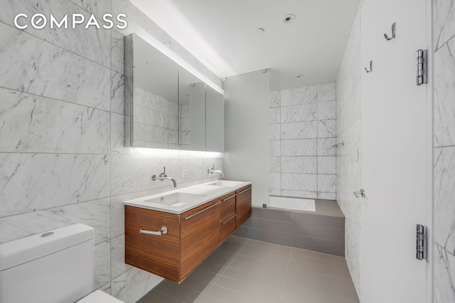 123 3rd Ave Unit 9C, New York City, NY 10003 - bathroom with tile walls, tiled bath, double vanity, toilet, and tile patterned flooring