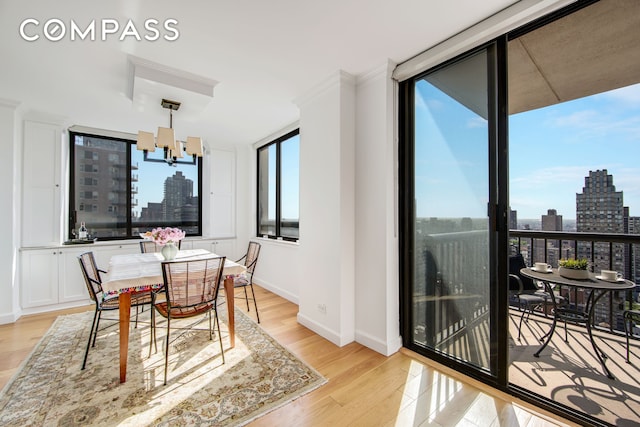 171 E 84th St Unit 31C, New York City, NY 10028 - dining space featuring a view of skyline, a chandelier, light wood-style flooring, baseboards, and ornamental molding