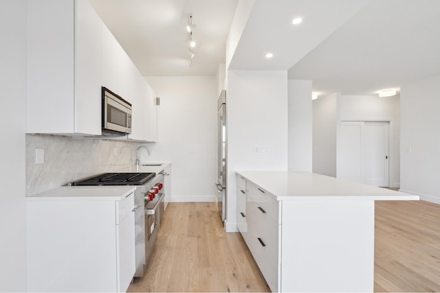 180 W End Ave Unit 30R, New York City, NY 10023 - kitchen featuring premium appliances, light wood finished floors, white cabinetry, backsplash, and light countertops