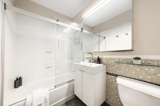 99 John St Unit 1112, New York City, NY 10038 - bathroom featuring vanity, shower / bath combination with glass door, toilet, tile walls, and tile patterned flooring