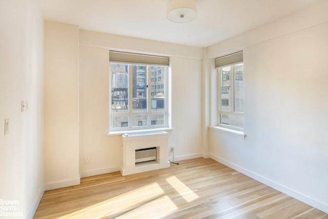 30 E 62nd St Unit 11A, New York City, NY 10065 - unfurnished room featuring light wood-type flooring, baseboards, a wall mounted air conditioner, and a fireplace