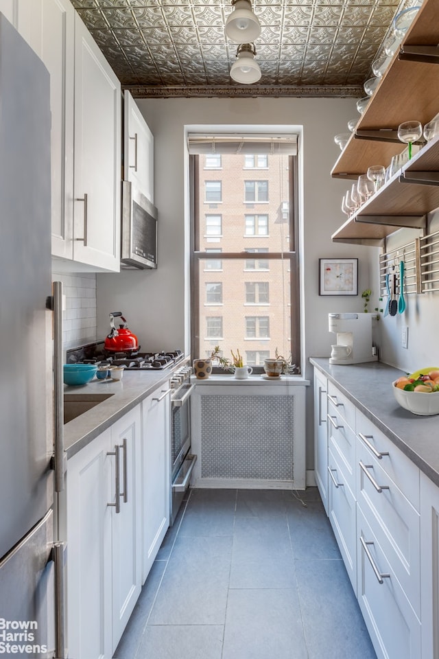 300 W 72nd St Unit 6E, New York City, NY 10023 - kitchen featuring stainless steel appliances, an ornate ceiling, white cabinets, tasteful backsplash, and light tile patterned floors