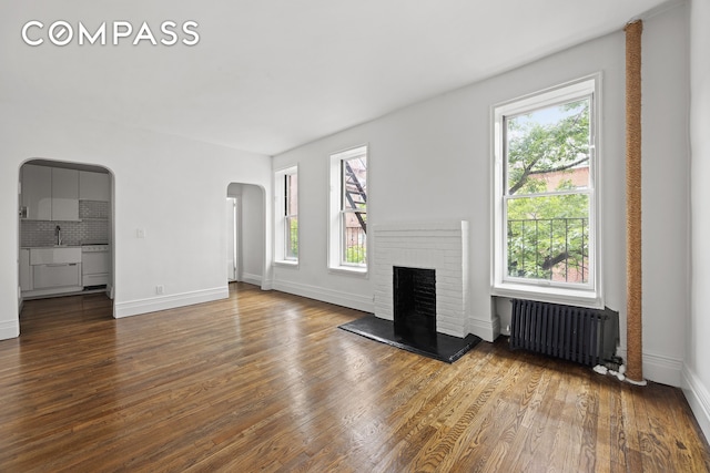 10 Bethune St Unit 2B, New York City, NY 10014 - unfurnished living room with radiator heating unit, arched walkways, wood finished floors, and a brick fireplace