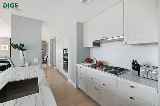389 E 89th St Unit 27A, New York City, NY 10128 - kitchen featuring stainless steel gas stovetop, light stone counters, decorative backsplash, under cabinet range hood, and white cabinetry