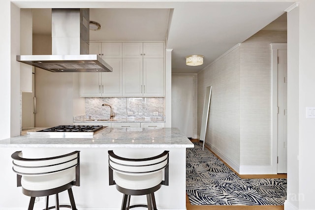 200 E 69th St Unit 28B, New York City, NY 10021 - kitchen featuring wall chimney range hood, stainless steel gas cooktop, white cabinetry, a peninsula, and a sink