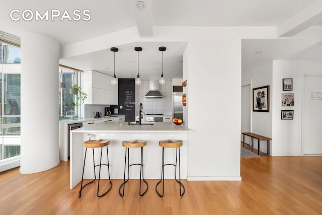 200 Chambers St Unit 25F, New York City, NY 10007 - kitchen with wall chimney range hood, a breakfast bar area, decorative backsplash, a peninsula, and light wood-style floors