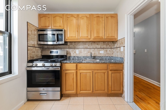 22-20 76th St Unit C3, New York City, NY 11370 - kitchen with appliances with stainless steel finishes, backsplash, dark stone countertops, and light tile patterned floors