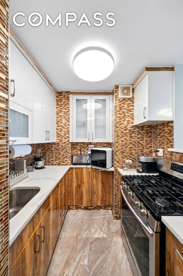 1360 Ocean Pkwy Unit 7B, New York City, NY 11230 - kitchen with stainless steel range with gas cooktop, white microwave, backsplash, light marble finish floors, and white cabinetry