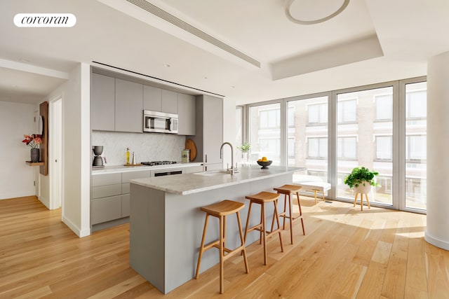 547 W 47th St Unit Ph8, New York City, NY 10036 - kitchen with gray cabinets, appliances with stainless steel finishes, light wood-style floors, a breakfast bar area, and light countertops