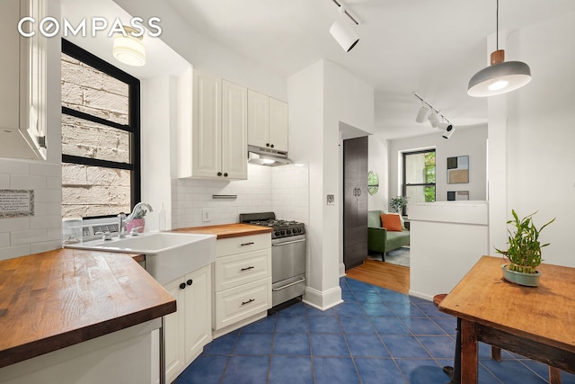 41 Perry St Unit 2A, New York City, NY 10014 - kitchen featuring butcher block counters, rail lighting, stainless steel range with gas cooktop, under cabinet range hood, and white cabinetry