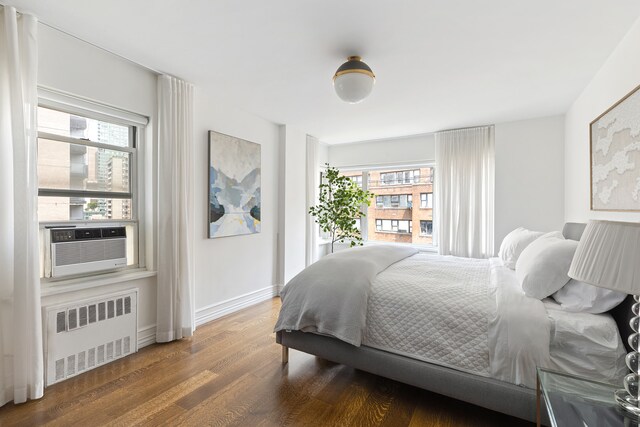 430 E 56th St Unit 11B, New York City, NY 10022 - bedroom featuring radiator heating unit, wood finished floors, and cooling unit