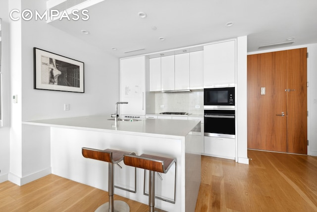 301 E 61st St Unit 12B, New York City, NY 10065 - kitchen featuring wall oven, black microwave, light wood-style floors, white cabinetry, and a breakfast bar area
