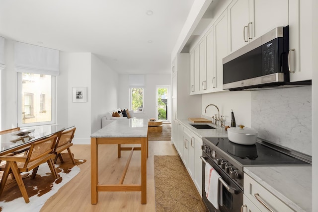 186 Clinton St Unit 4B, New York City, NY 11201 - kitchen featuring stainless steel appliances, light wood-style flooring, white cabinetry, open floor plan, and light stone countertops