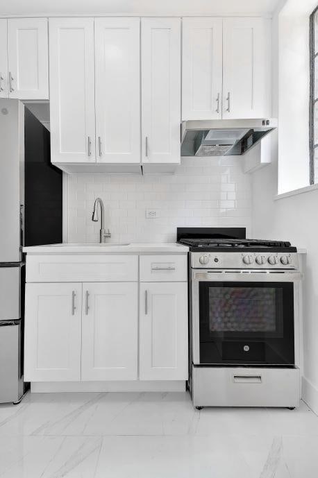 10 Park Ave Unit 4-C, New York City, NY 10016 - kitchen with gas stove, under cabinet range hood, white cabinets, light marble finish floors, and freestanding refrigerator