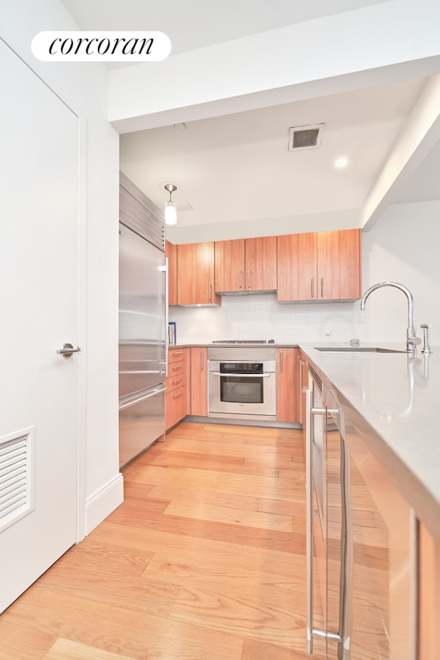 125 W 22nd St Unit 9B, New York City, NY 10011 - kitchen featuring stainless steel appliances, light wood-style flooring, light countertops, and decorative backsplash